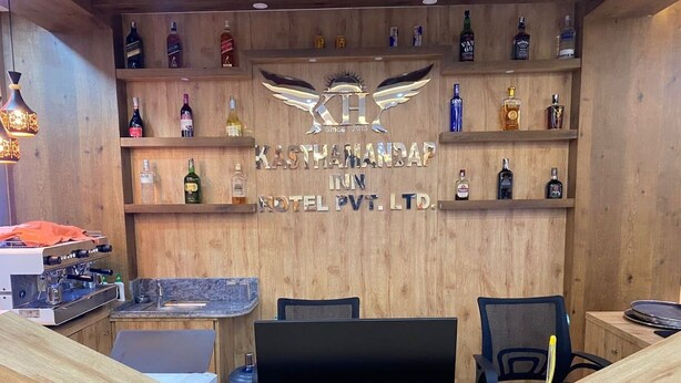 Baarialue, jossa on puuhyllyt, joilla on esillä erilaisia alkoholijuomapulloja, siinä on siivekäs logo ja teksti: ”KASTHAMANDAP IN HOTEL PVT. LTD.”