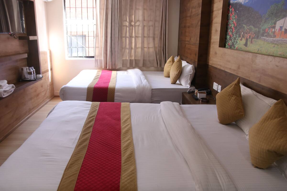 A hotel room with two beds, a wooden headboard, a painting on the wall, and a window with curtains.