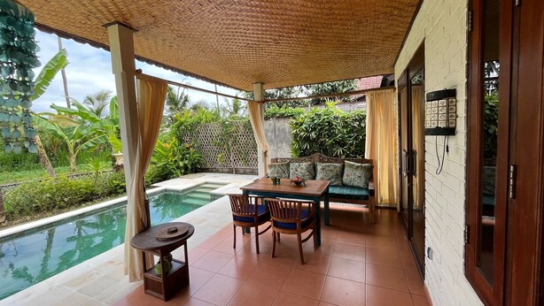 Uma área externa coberta com piscina, uma mesa com cadeiras e um sofá.