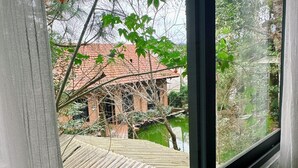A view through a window of a building with a red-tiled roof, a brick wall, and a wooden deck. - Dalat Zen Homestay (3 Bao Loc)