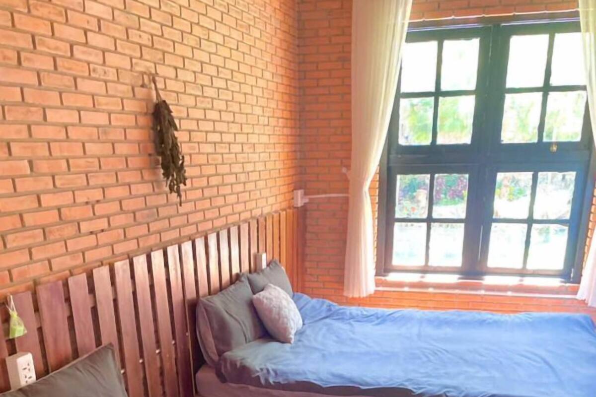 A room with two beds, a brick wall, and a window with curtains.