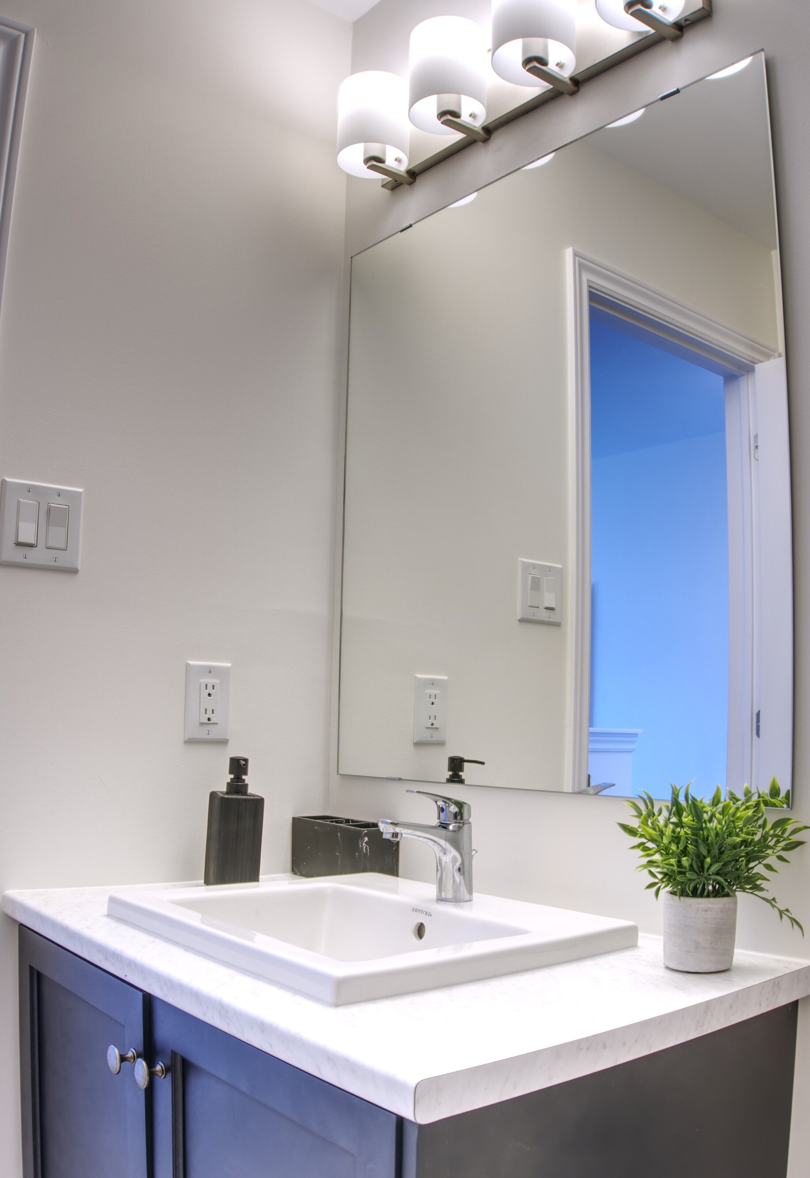A modern bathroom with a white sink, a large mirror, and a potted plant.