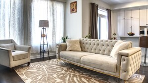 A living room with a beige sofa, a side chair, a patterned rug, and a floor lamp. - Spacious and Cozy Room with Private Bathroom in a house with WiFi, AC in Ottawa. (Ottawa)