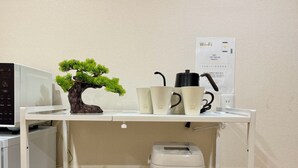 Een kitchenette met een magnetron, een koffiezetapparaat, een rijstkoker en een kleine bonsaitje.