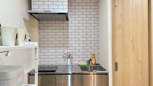 Een compacte keuken met een roestvrijstalen afzuigkap, een witte bakstenen spatwand en een houten deur.