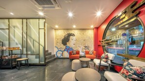 A modern interior with seating areas, a mural, and a large window with a view of the street. - U Tor Yaowarat (Bangkok)