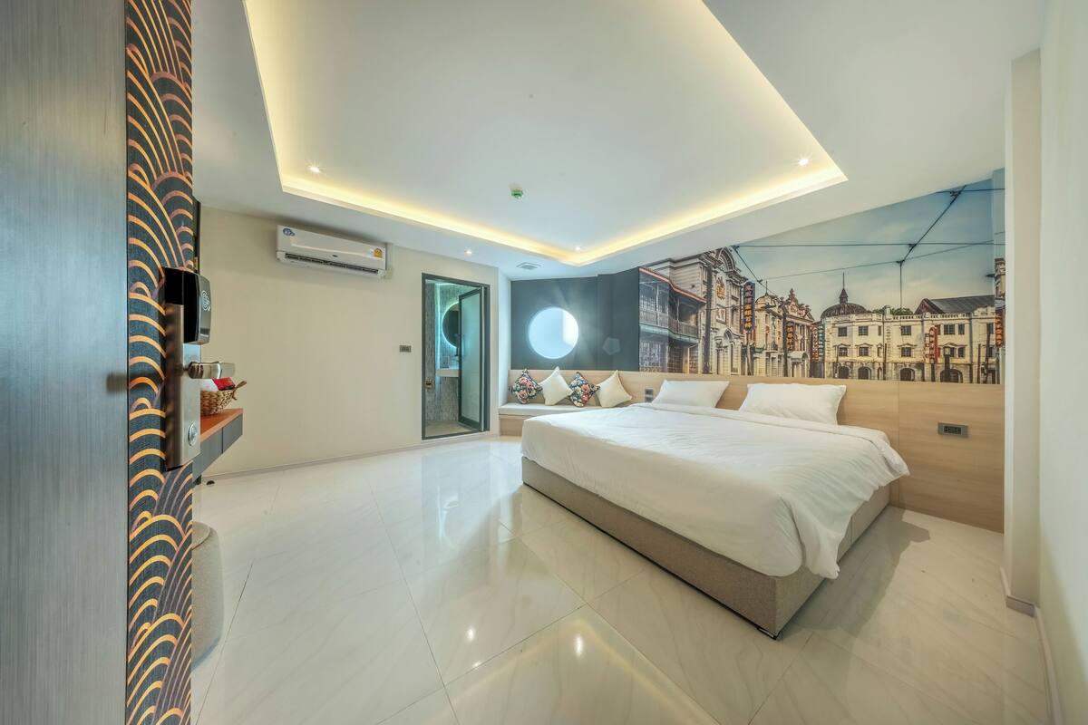 A modern hotel room with a large bed, a cityscape mural, a built-in air conditioning unit, and a unique patterned door.