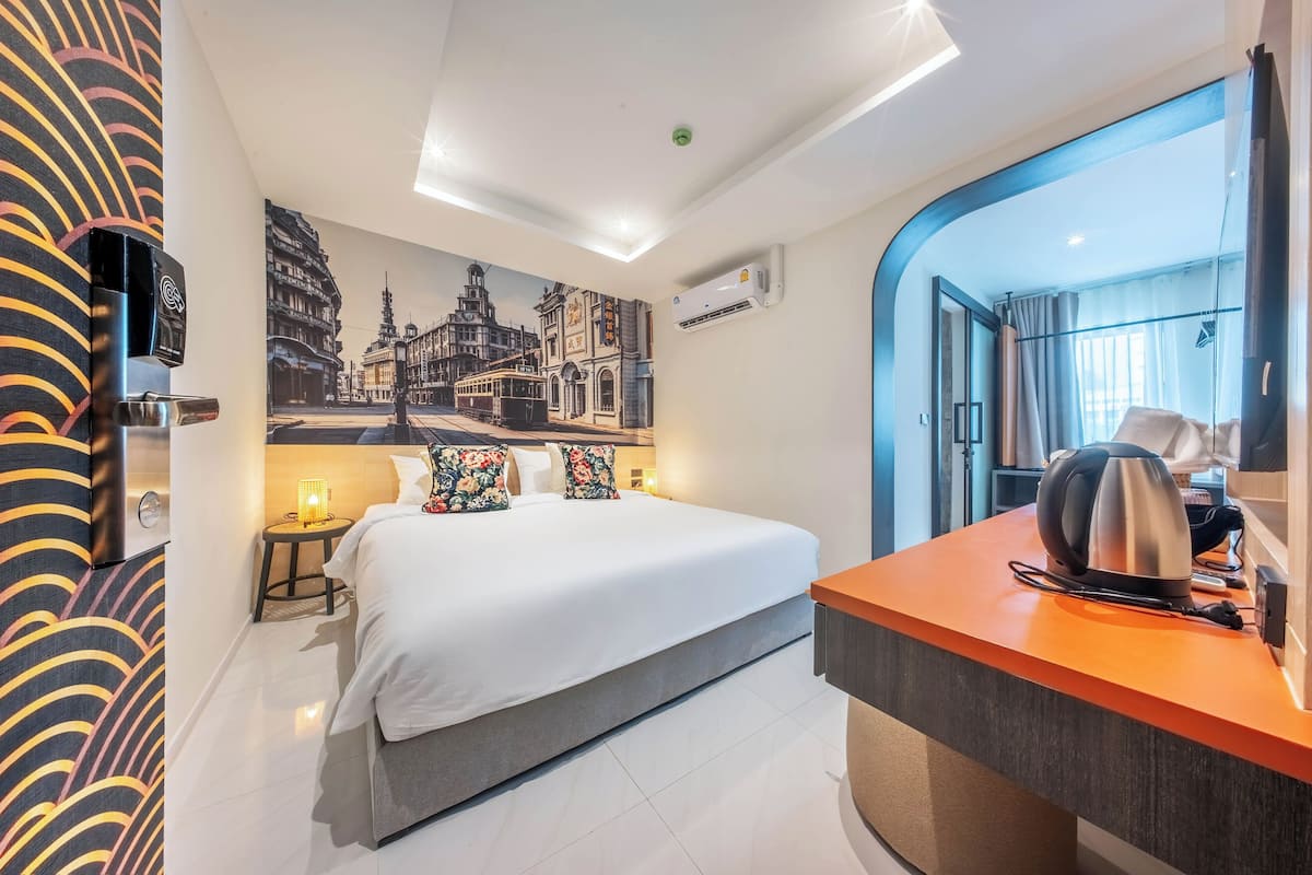 A hotel room with a bed, a desk, a coffee maker, and a wall mural.