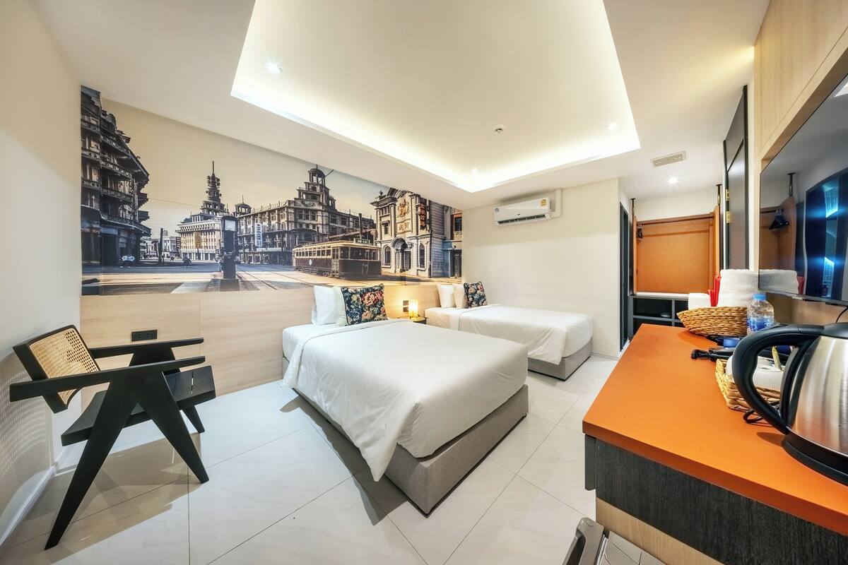 A hotel room with two beds, a desk, a TV, and a mural of a cityscape.