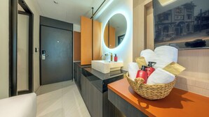 A modern bathroom with a black marble countertop, a white sink, a round mirror with a light, and a basket of toiletries. - U Tor Yaowarat (Bangkok)