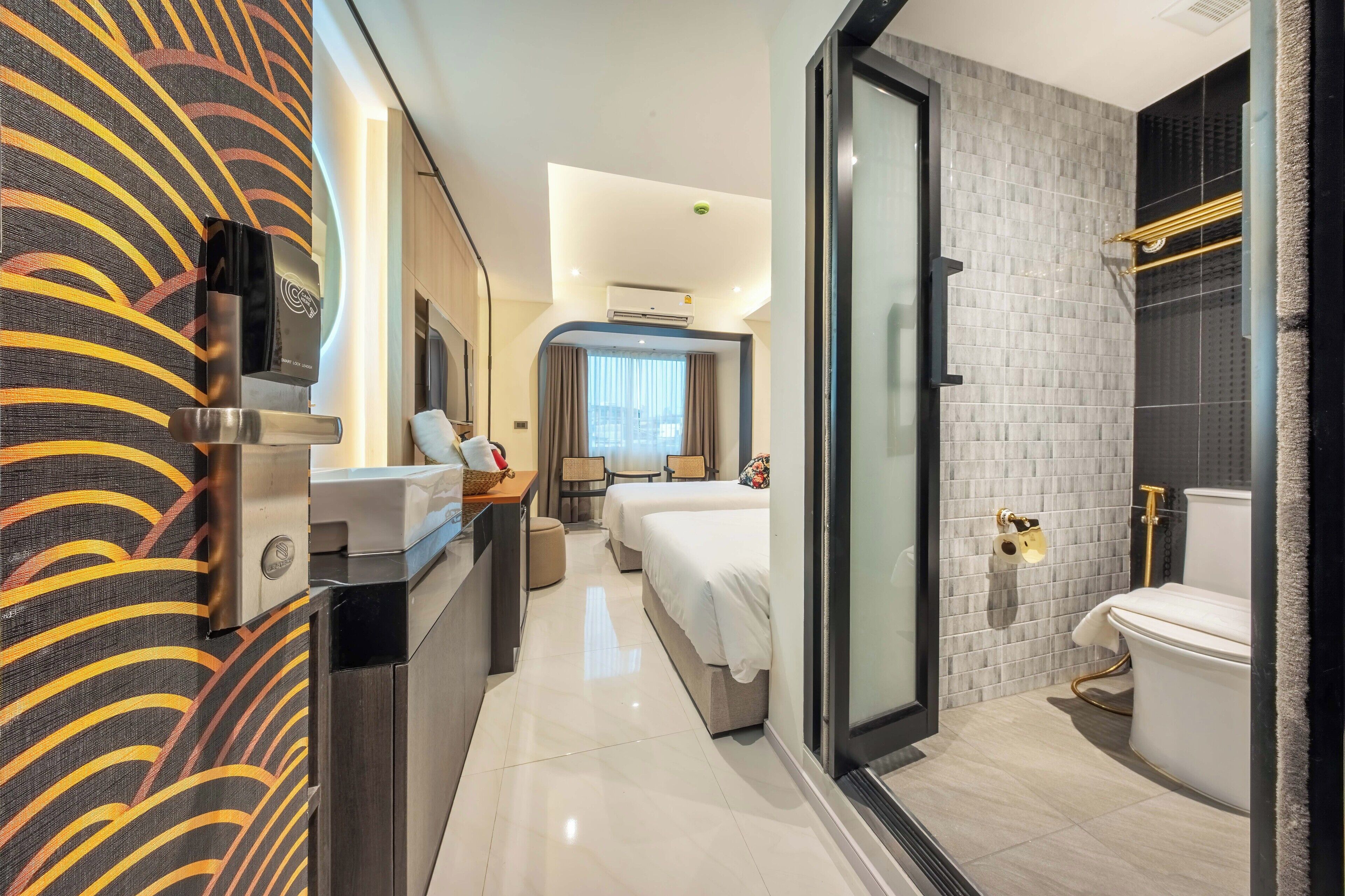 A modern hotel room with a kitchenette, two beds, a bathroom with a toilet and shower, and a view of the city.