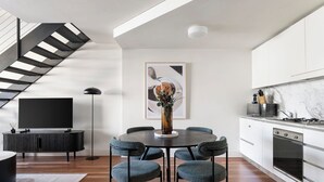 A modern kitchen with a dining area, a flat-screen TV, and a staircase.