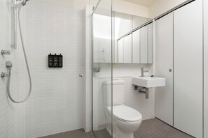 A modern bathroom with a glass-enclosed shower, a white toilet, and a sink with a mirror above it. - Crown Street Apartments by Urban Rest (Surry Hills)