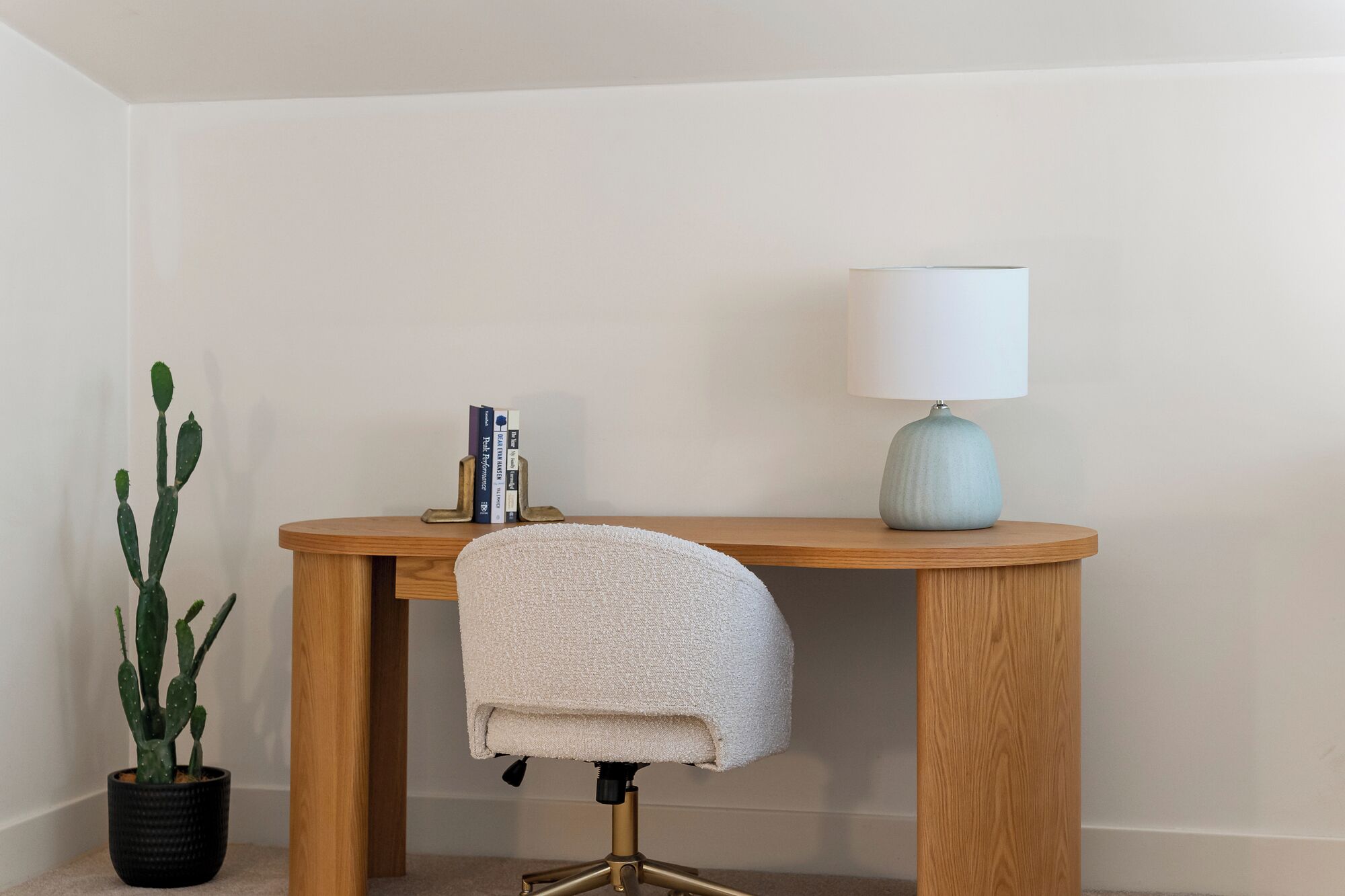 A wooden desk with a lamp, a chair, and a cactus plant.