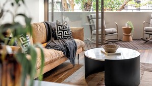 A cozy living area with a sofa, a coffee table, and a rocking chair. There is a large window providing a view of the outdoors.