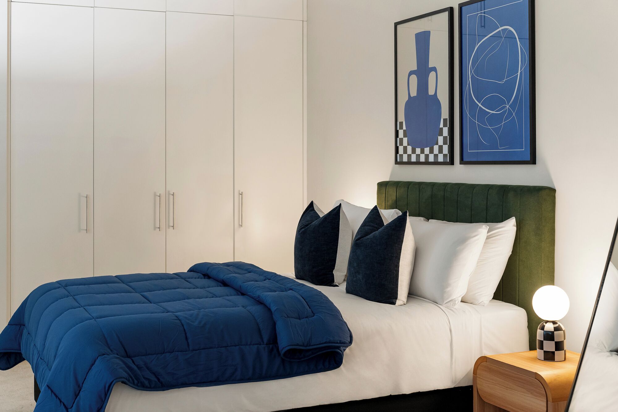 A bedroom with a bed, pillows, a bedside table with a lamp, and a wardrobe.