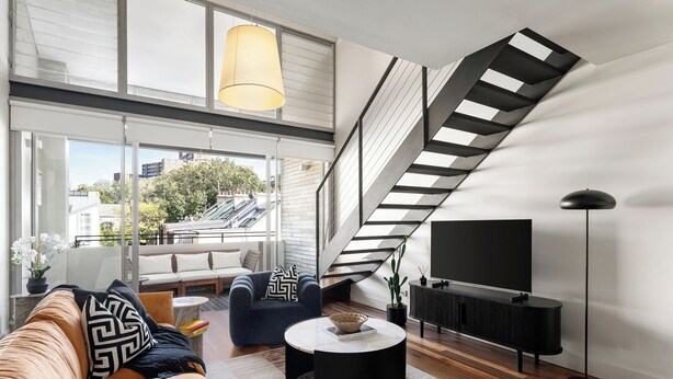 A modern living room with a staircase, a sofa, a coffee table, and a TV.