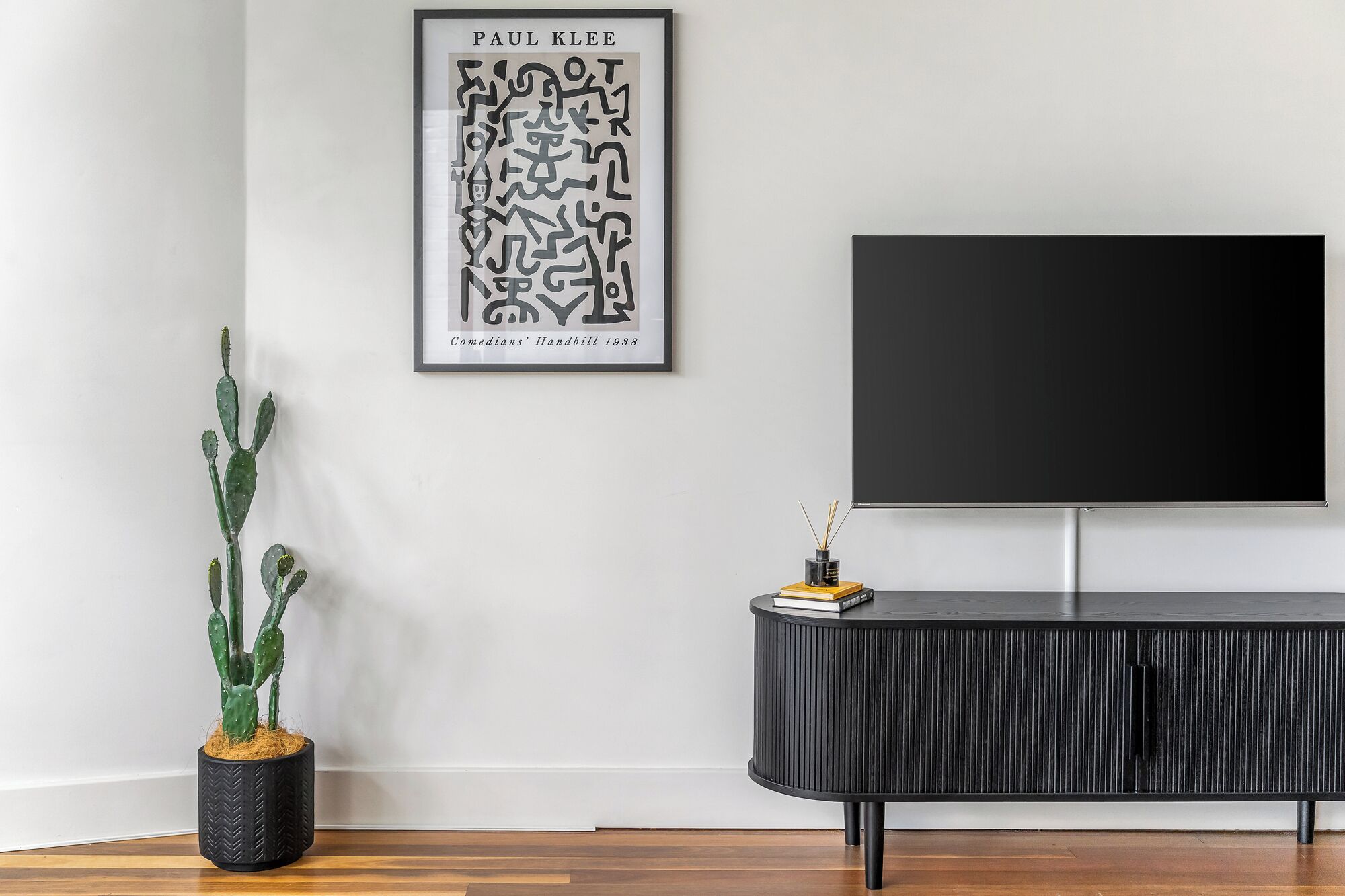 Una sala moderna con un mueble de televisión negro, una planta de cactus y una obra enmarcada en la pared.