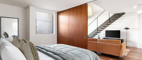 Quarto moderno com cama, sofá, televisão e escada.
