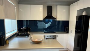 A modern kitchen with white cabinets, a black stove, and two wooden stools. - 21A Boab Cottage (Mayfield)