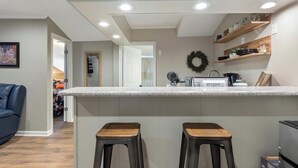 Una cocina moderna con encimera blanca, dos taburetes de madera y horno empotrado.