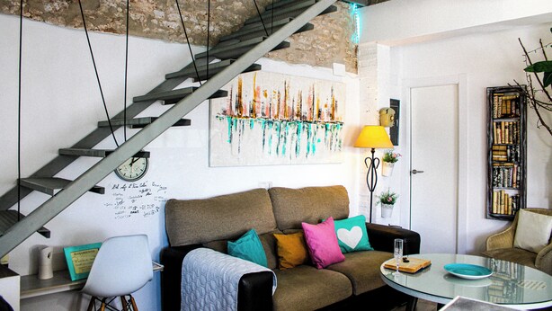 Una sala de estar con una escalera, un sofá, una mesa de centro y una estantería.