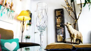Un vaso transparente sobre una mesa, un libro, una lámpara, una estantería y una estatua decorativa de oveja.