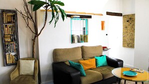Una sala de estar con un sofá, una mesa de centro de vidrio, una estantería y una planta grande.