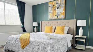 Un lit bien fait, recouvert d’une couvre-lit à motifs, avec deux lampes de chevet et un tableau décoratif au-dessus du lit.