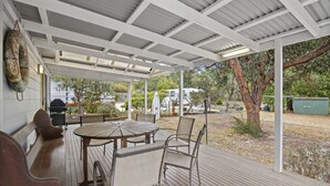 Une terrasse couverte avec une table et des chaises en bois, un barbecue et une vue sur le jardin arrière.