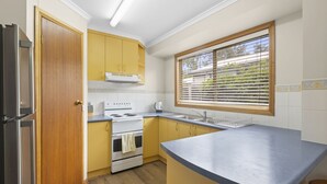 Une cuisine de taille réduite avec des meubles de couleur jaune, une cuisinière blanche et une fenêtre équipée de stores.