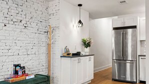 A modern kitchen with white cabinets, a stainless steel refrigerator, and a green sofa. - Sleeps 12, Mxn Streets (Pittsburgh)