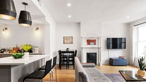 A modern living room with a sofa, a dining area with a table and chairs, a kitchen with a bar area, and a fireplace. - Sleeps 12, Mxn Streets (Pittsburgh)