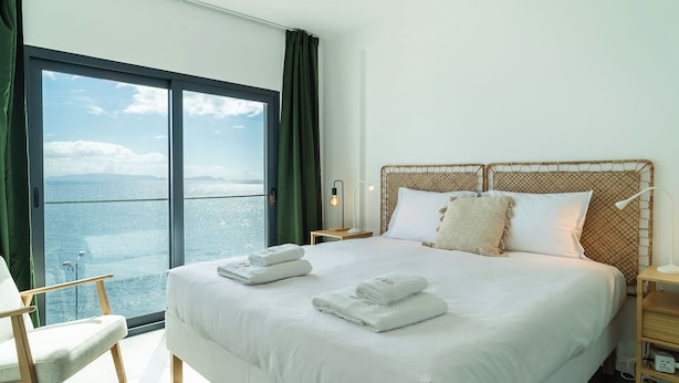 A hotel room with a large window offering a view of the sea, a bed with white linens, and a ceiling fan. - GuestReady - Endless Ocean Views (Santa Cruz)