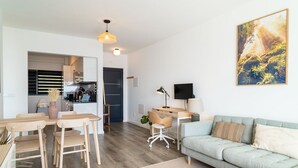 A modern living room with a light blue sofa, a dining area with wooden furniture, a kitchen visible through an open door, and a large painting on the wall. - GuestReady - Endless Ocean Views (Santa Cruz)