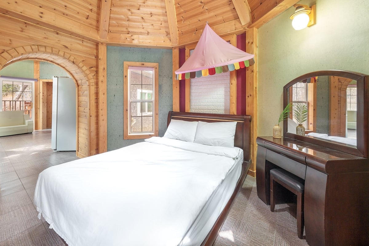 Ein Zimmer mit Holzboden, einem Bett, einer Kommode und einem Spiegel.