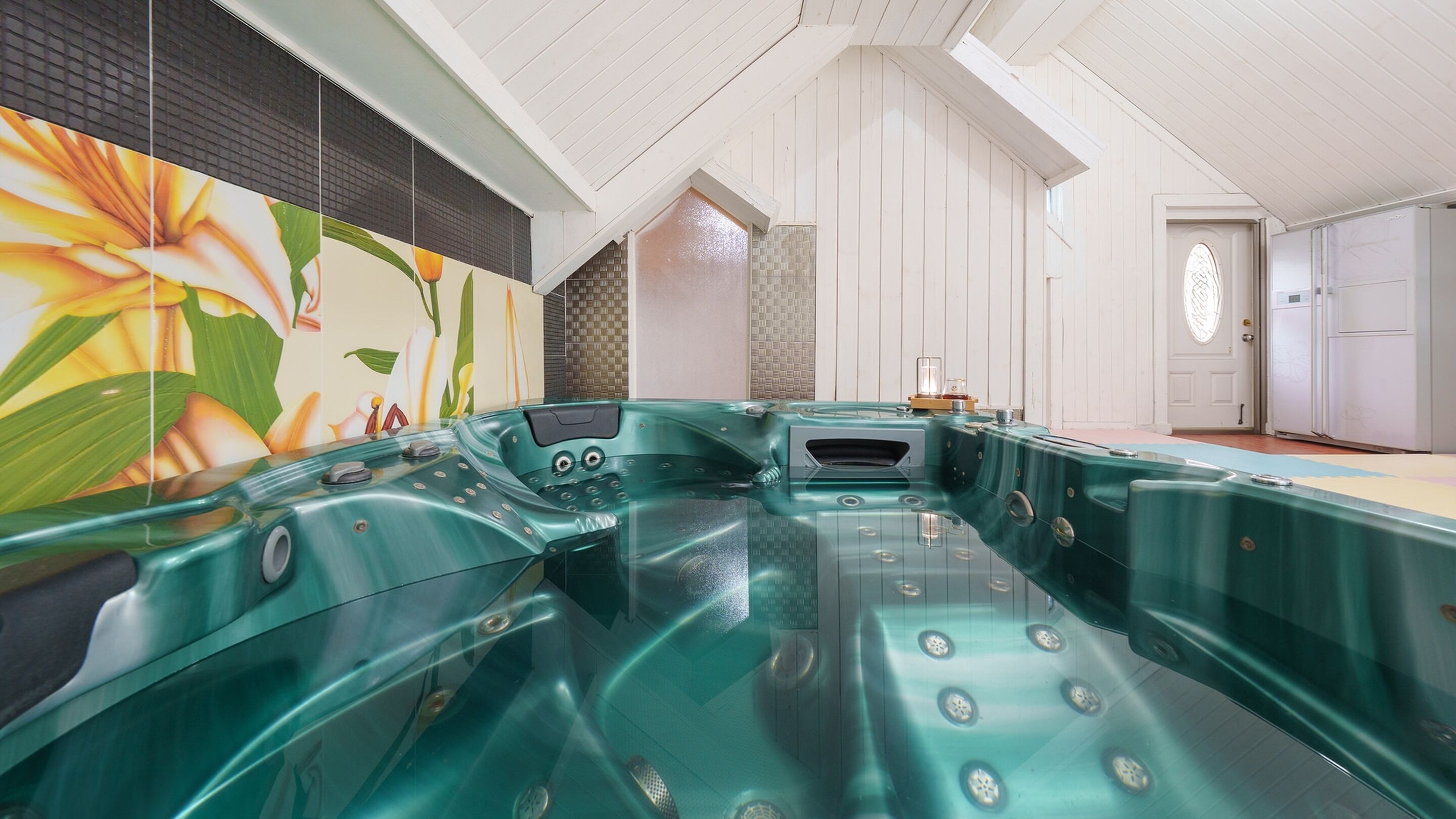 Un área de spa con un jacuzzi grande, una pared con un mural floral y una puerta blanca.