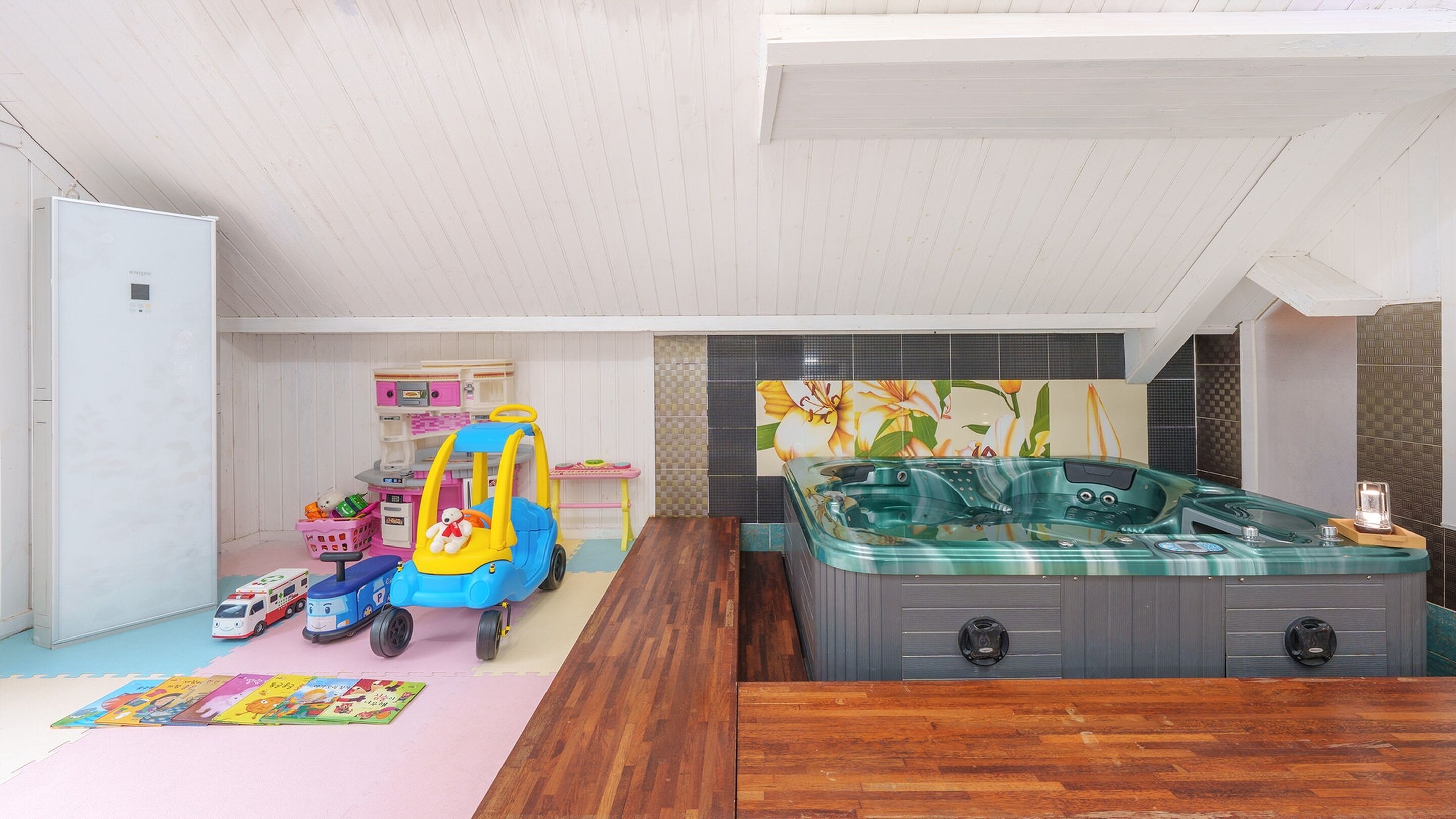 Een kamer met houten vloer, een bubbelbad, een speelgoedauto en een speelruimte met speelgoed en een mat.
