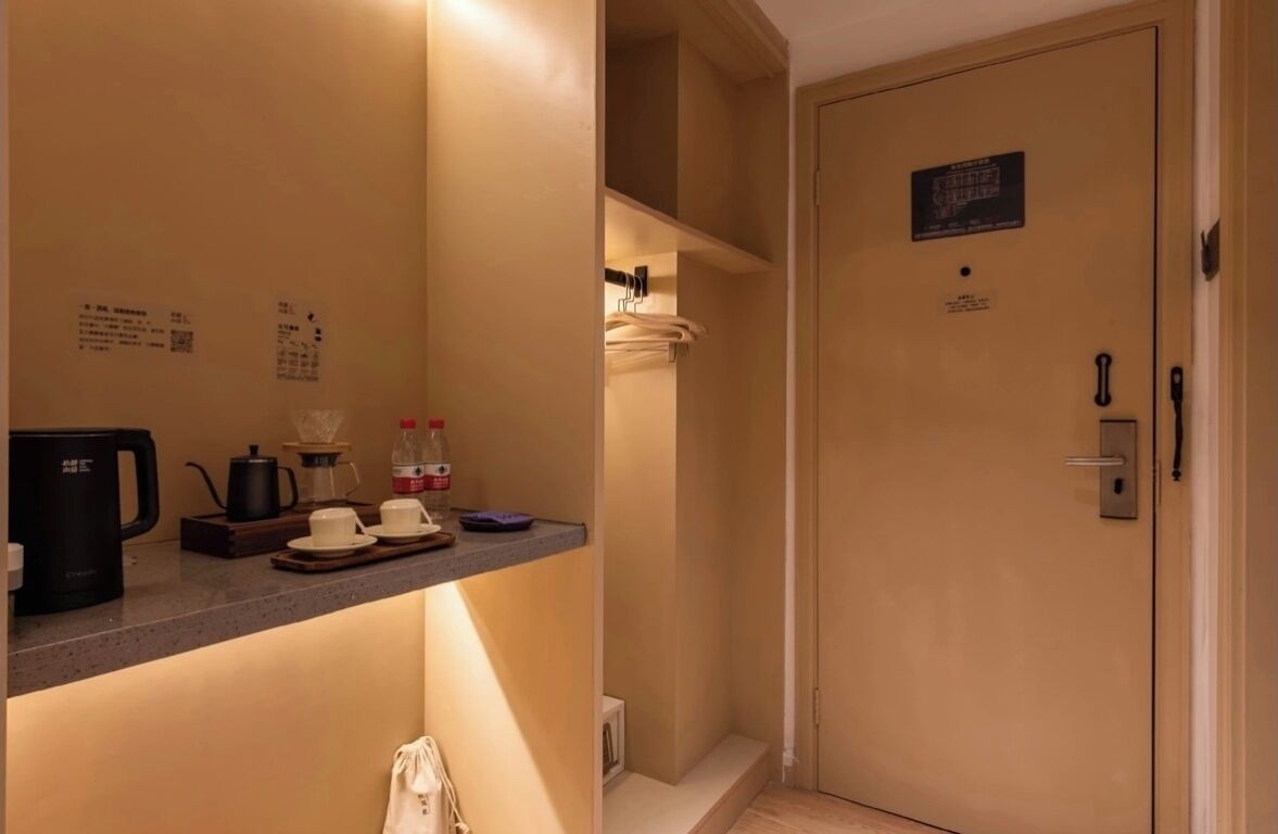 A hotel room with a kitchenette area, a door with a sign, and a towel rack.