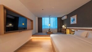 A hotel room with a large bed, a desk, a chair, a window with curtains, a wall-mounted TV, and a small table with a lamp. - SHIJING HOTEL (Guangzhou)