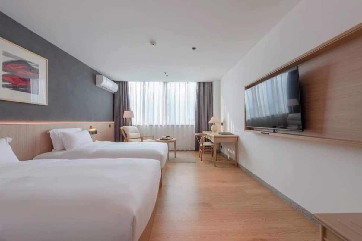 Habitación de hotel con dos camas, un escritorio, televisor y un ventanal con cortinas.