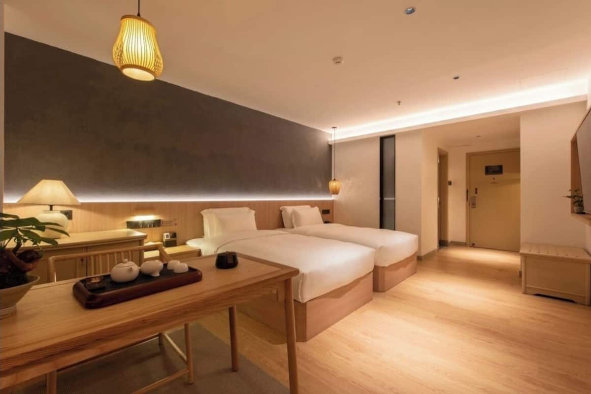 Una habitación de hotel moderna con suelo de madera, una cama grande, mesitas de noche, un escritorio con una bandeja de té y una lámpara colgante.