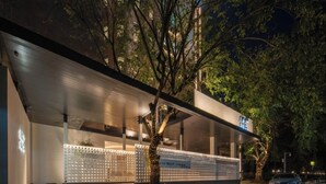 A modern building with a covered entrance, a tree in front, and a car parked nearby. - SHIJING HOTEL (Guangzhou)