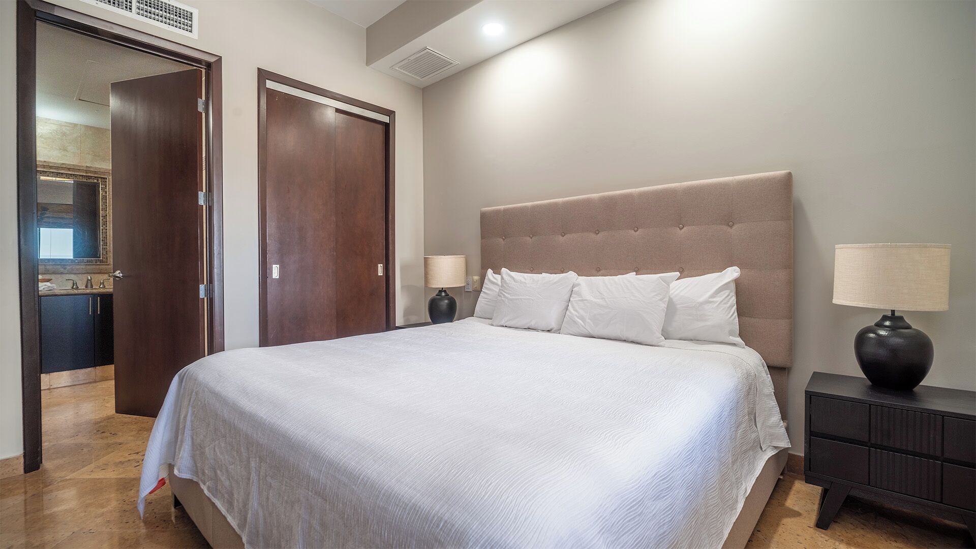 A hotel room with a large bed, two bedside tables, a nightstand, and a wardrobe.