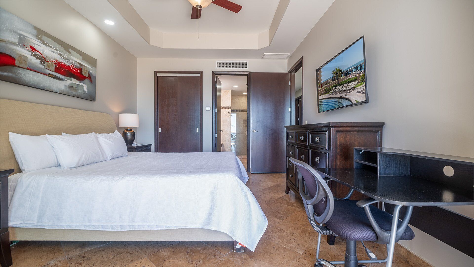 A hotel room with a bed, desk, chair, and artwork on the walls.