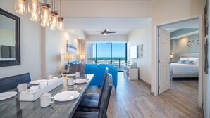 A modern hotel room with a dining area, a balcony with a view of the ocean, and a separate bedroom.