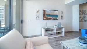 A modern living room with a large window, a sofa, a coffee table, and a painting of a beach scene.