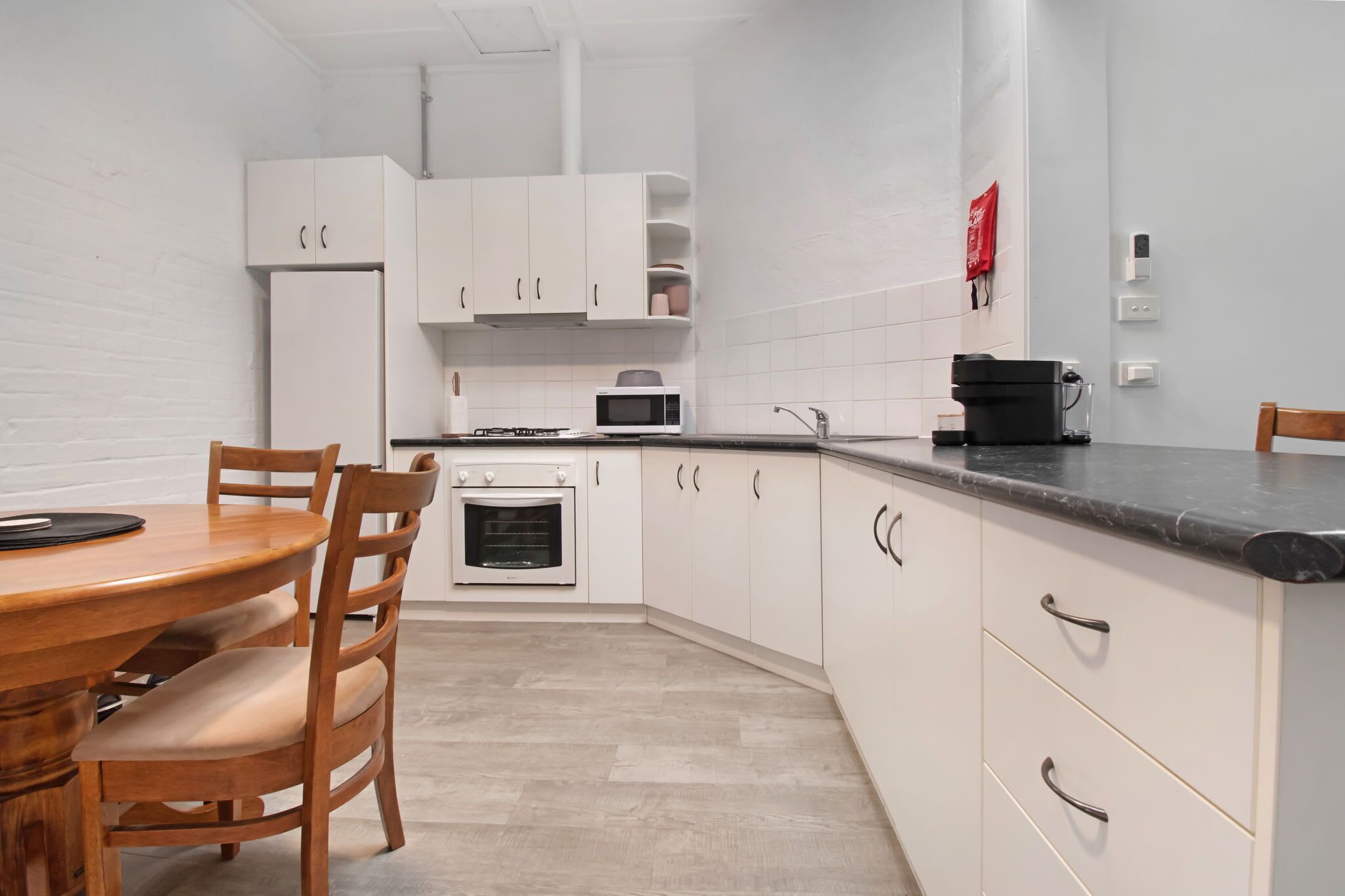 Une cuisine moderne avec des meubles blancs, une table à manger en bois et un four encastré.