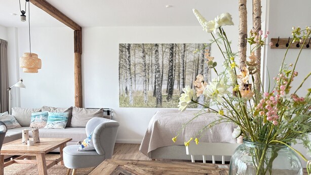 Ein gemütliches Wohnzimmer mit einer Couch, einem Couchtisch und einem großen Fenster mit Blick auf einen Wald.