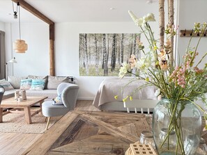 A cozy living room with a sofa, a coffee table, and a large window with a forest view. - Stuuv 8 - Vacation in the 1st row - with Baltic Sea view and direct beach location (Scharbeutz)